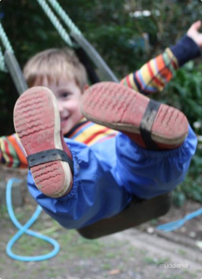 Boy plays on swing wearing blue muddlarks® pants and showing shoe straps