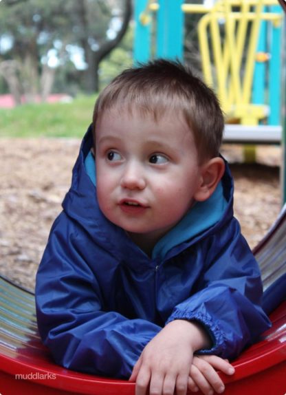 Boy playing in red tunnel wearing blue waterproof muddlarks® puggle jacket