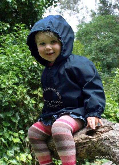 Girl wearing navy blue waterproof muddlarks® puggle rain jacket with hood on