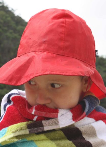 Boy wearing red muddlarks® sou'wester rain hat and wrapped in towell